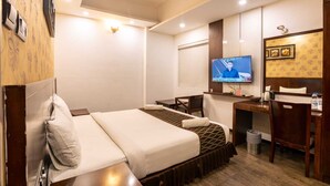 Habitación de hotel con cama, escritorio, silla, televisor y un cesto de basura.