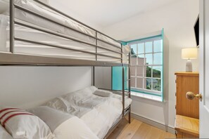 A bunk bed room with a window, a wooden cabinet, and a lamp. - Windermere House - Sea Views Close to Harbour (Tenby)