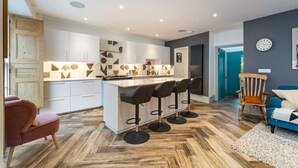 A modern kitchen with a central island, bar stools, and a wooden floor. - Windermere House - Sea Views Close to Harbour (Tenby)