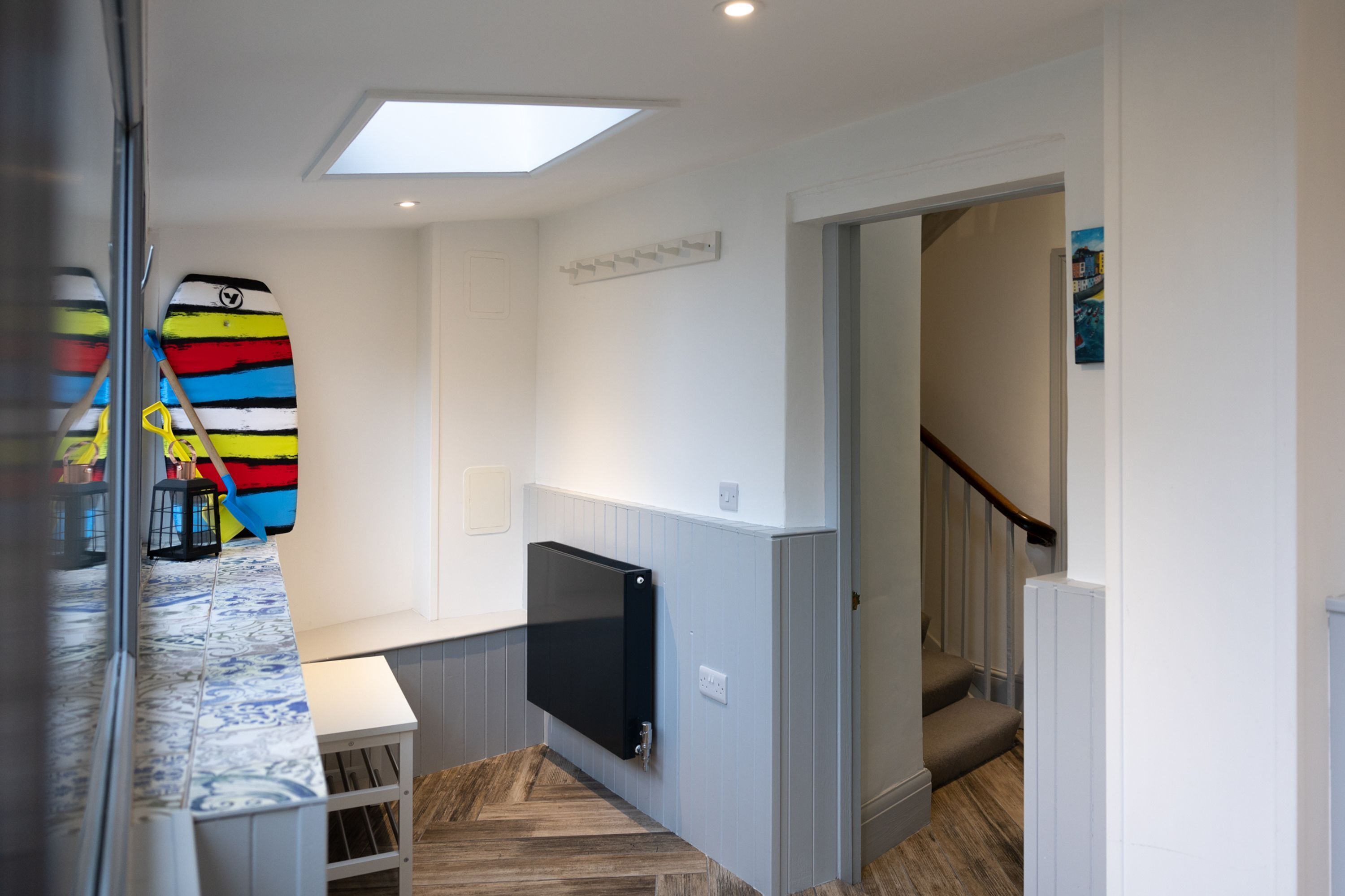 A modern interior with a flat-screen TV mounted on the wall, a staircase leading to another level, and a colorful surfboard leaning against the wall.