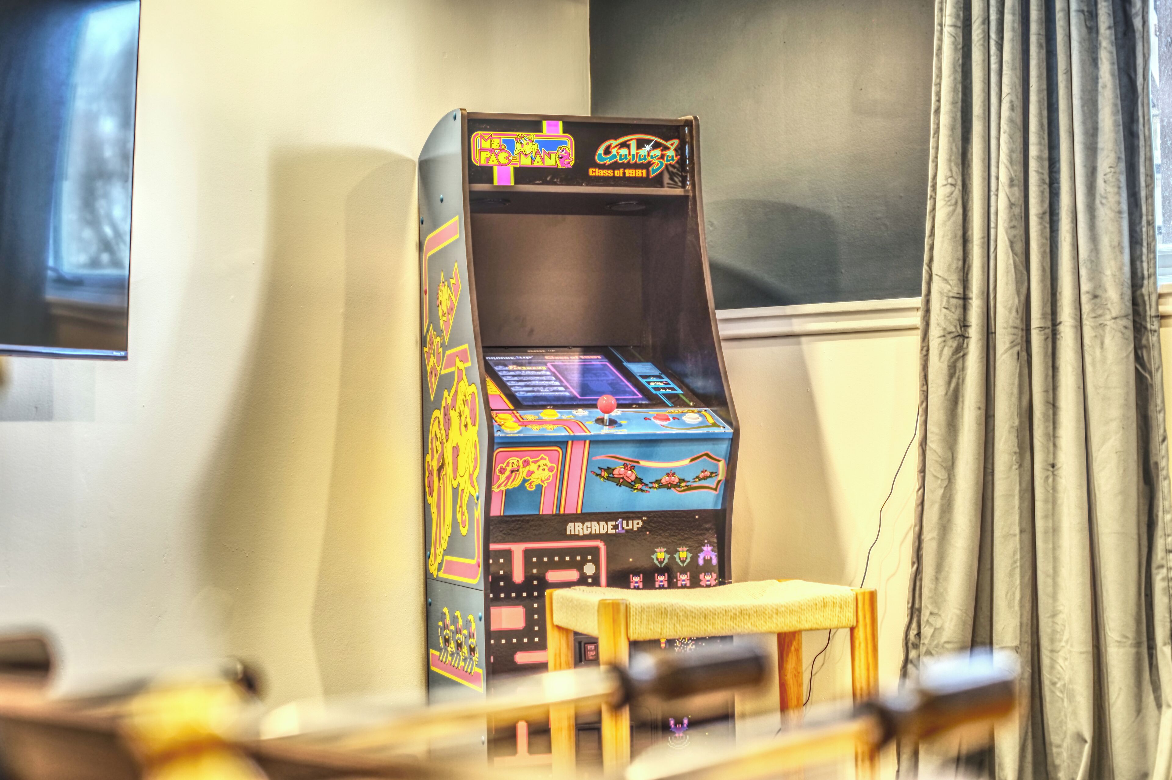 Une vieille borne d’arcade dans une pièce avec une fenêtre et des rideaux.