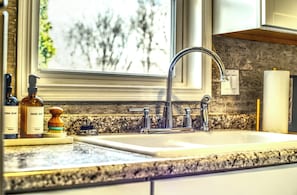 Una cocina con encimera de granito, grifo de acero inoxidable y ventana con vistas a árboles.