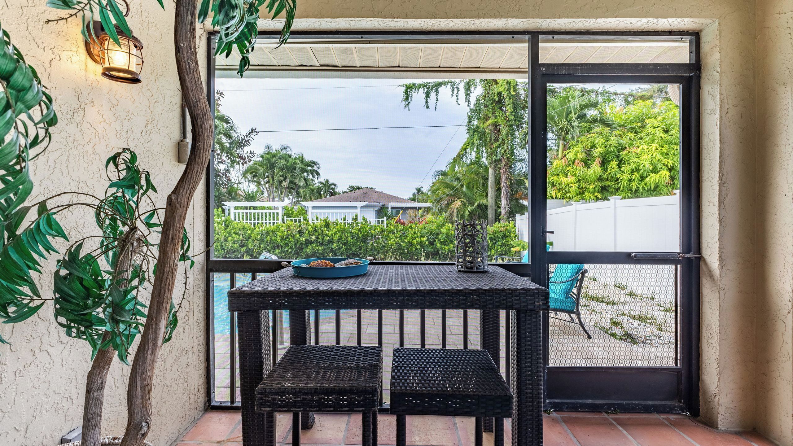 A balcony with wicker furniture, a table with a blue bowl, and a view of a white house and greenery.