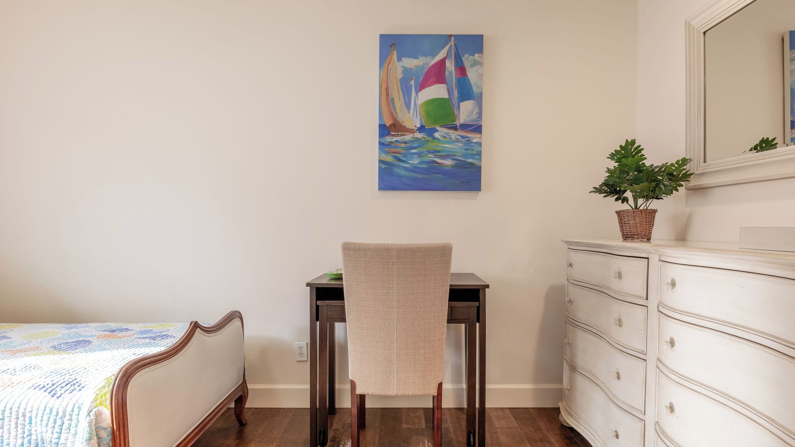 Quarto com cama, escrivaninha, cadeira, cômoda e pintura de veleiros.