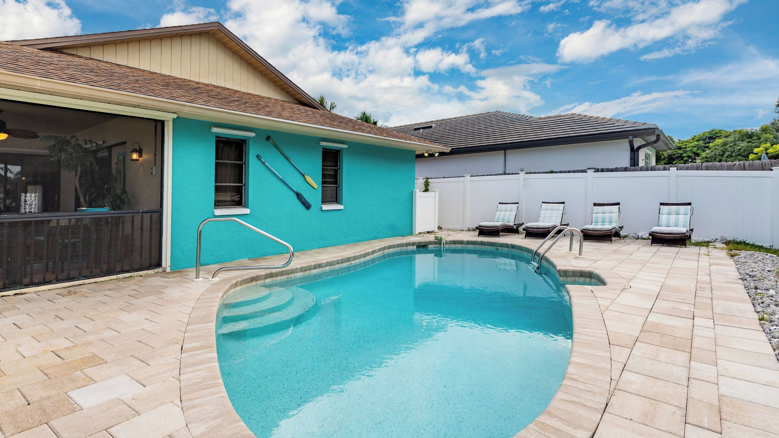 A swimming pool with a curved edge, a covered patio area, and a white fence.