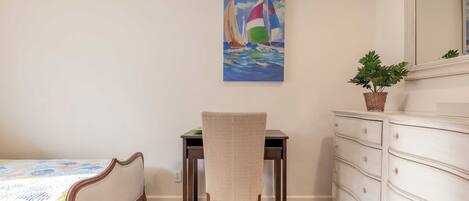 A bedroom with a bed, a desk, a chair, a dresser, and a painting of sailboats on the wall.
