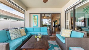 Een ruim terras met een blauwe zithoek, een houten tafel en uitzicht op het interieur door een glazen deur.