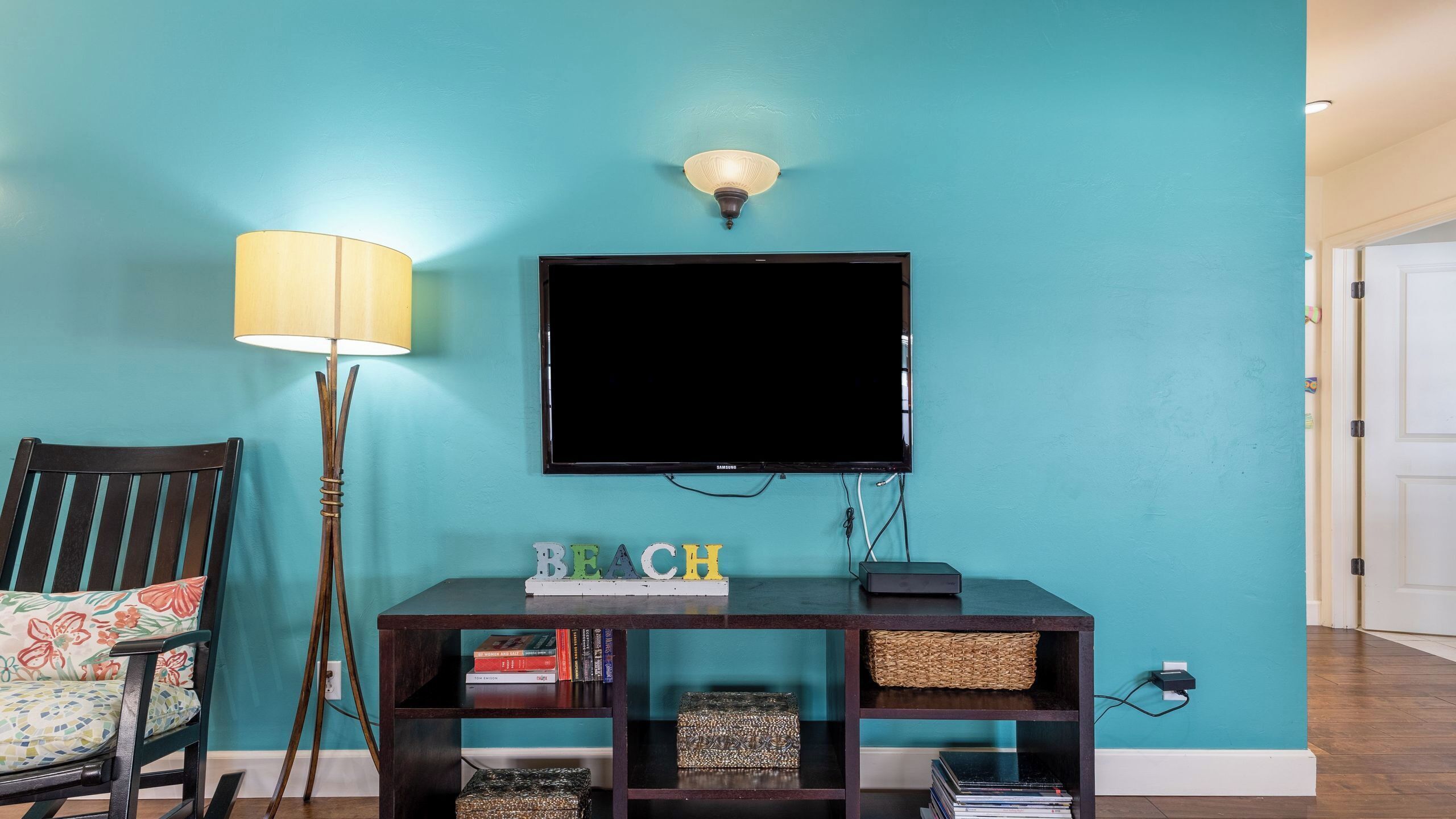 Um quarto com paredes azul-esverdeadas e uma televisão de tela plana presa acima de um console de madeira escura.