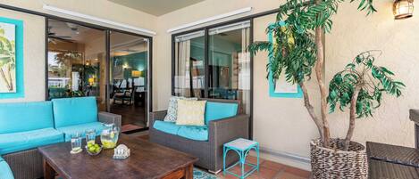 A spacious patio area with a blue sofa, a wooden table with drinks, and a large potted plant.