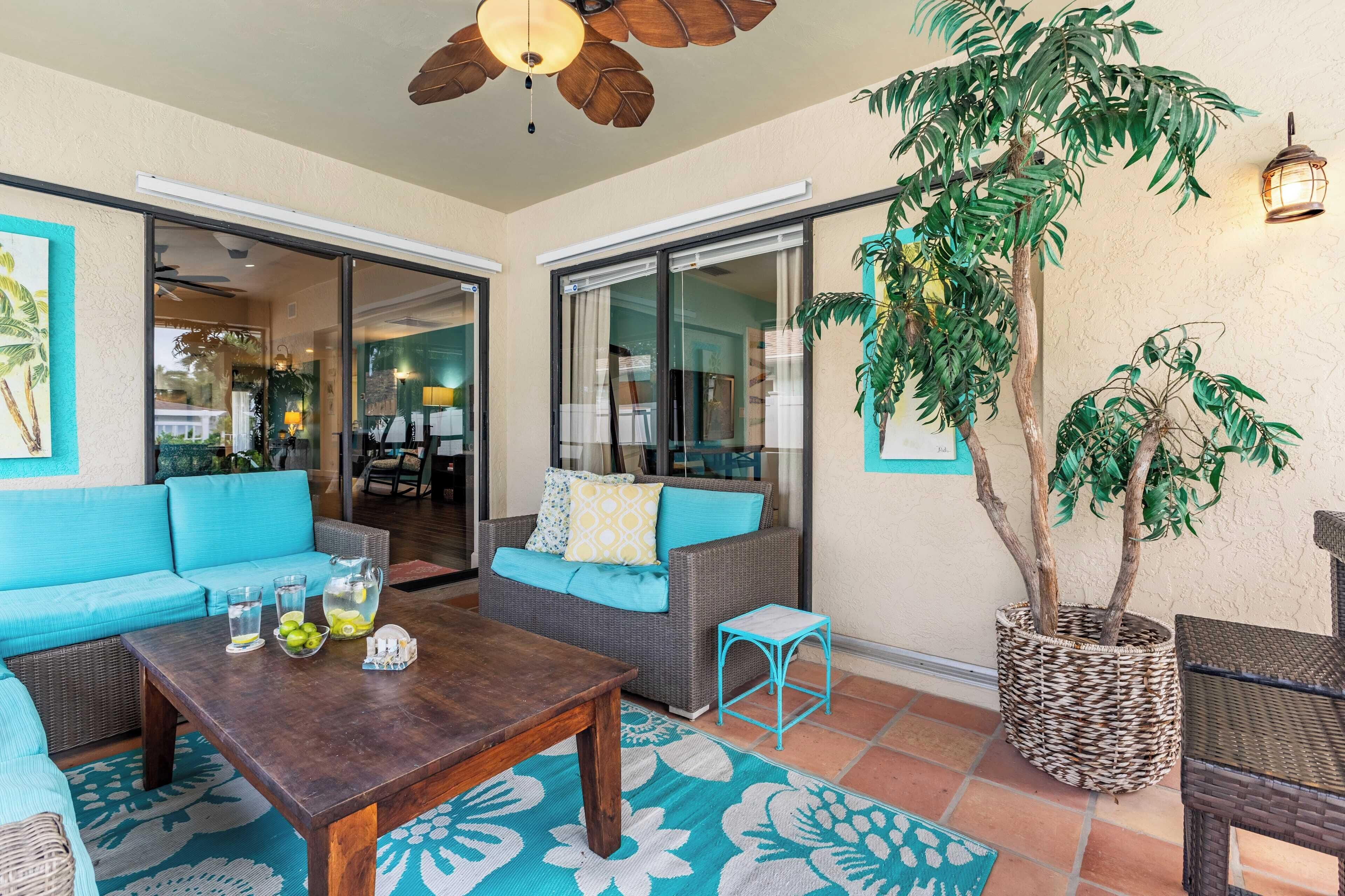 A spacious patio area with a blue sofa, a wooden table with drinks, and a large potted plant.