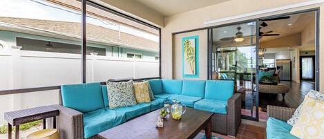 A spacious balcony with a blue sofa, wicker furniture, and a wooden coffee table.
