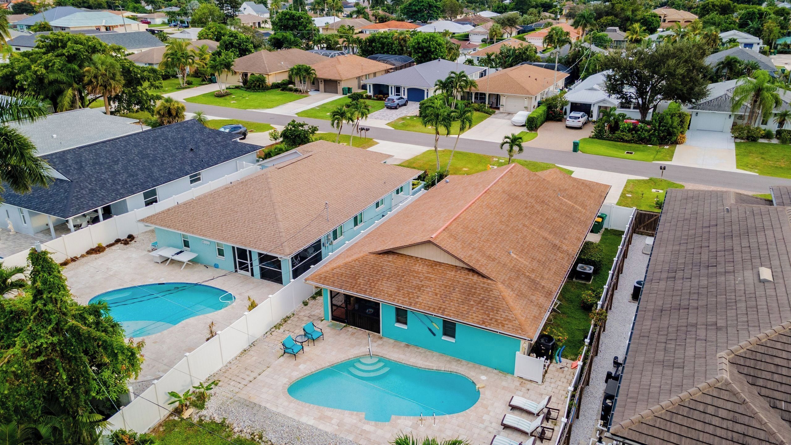 Zona residencial con dos casas que incluyen piscinas, rodeada de vegetación y otras viviendas.