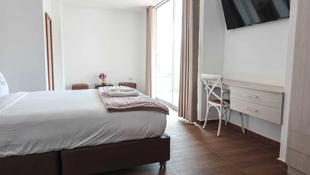Een hotelkamer met een groot bed, een bureau met lades, een stoel, een aan de muur bevestigde televisie en een raam met gordijnen.