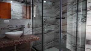 A bathroom with a marble wall, a glass shower enclosure, a sink, and a wooden cabinet.