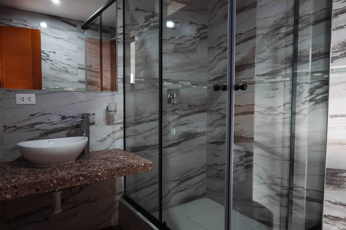 A bathroom with a marble wall, a glass shower enclosure, a sink, and a wooden cabinet.