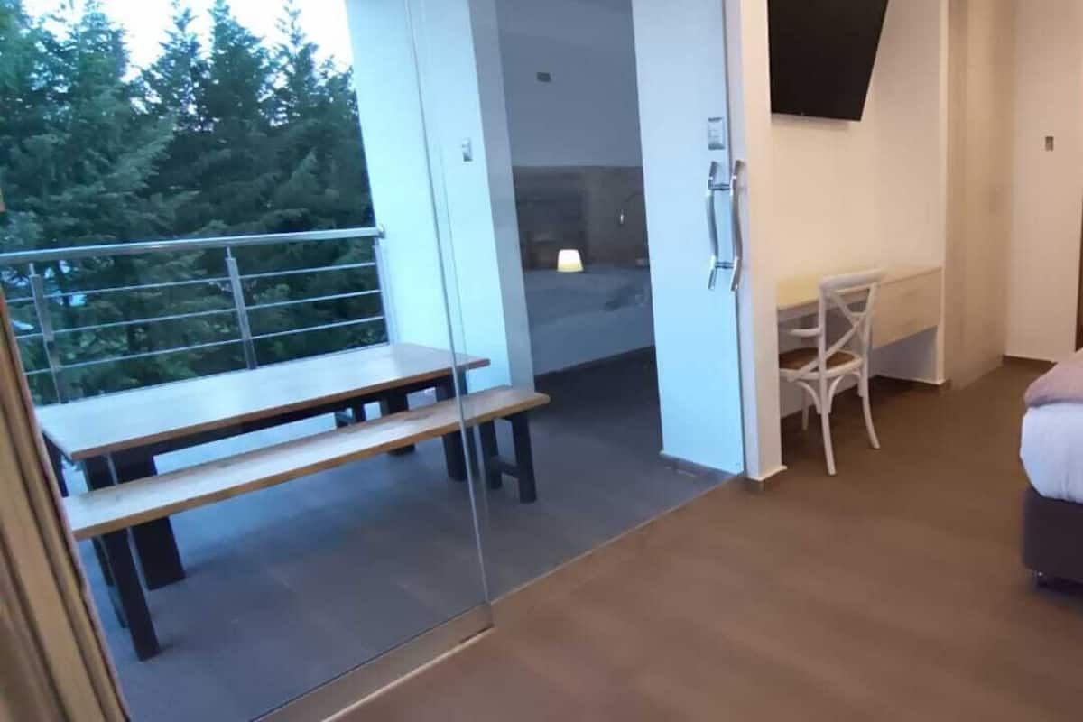 A bedroom with a bed, a desk, and a chair. There is a balcony with a table and chairs.
