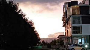 Een modern meerlaags gebouw met balkons en grote ramen, omringd door een gazon en bomen.