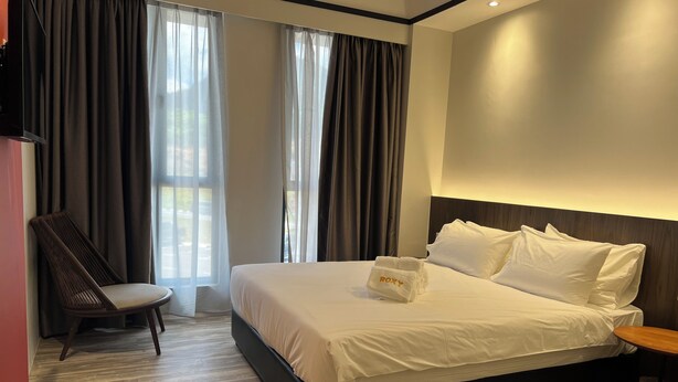 Habitación de hotel con una cama grande, una silla, una mesita de noche y vistas al exterior a través de la ventana.