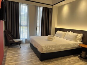 A hotel room with a large bed, a chair, a bedside table, and a view of the outdoors through the window. - Roxy Hotel Siniawan  (Kuching)