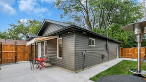 A single-story house with a covered patio area, a small table and chairs, and a wooden fence in the background.