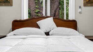 A neatly made bed with white bedding and a wooden headboard, positioned in front of a window with a view of trees.