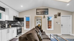 A modern kitchen with white cabinets, a stainless steel range hood, and a black microwave.