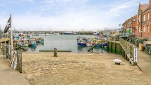 Un puerto con barcos amarrados, un paseo marítimo adoquinado y un edificio con un letrero que dice "Queen Ferry".