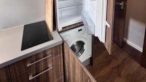 A compact kitchen with a built-in washing machine, wooden cabinetry, and a small countertop. - London Studio Retreat - Colney Hatch Lane (London)