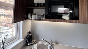A modern kitchen with dark wood cabinets, a stainless steel sink, and a black microwave. - London Studio Retreat - Colney Hatch Lane (London)
