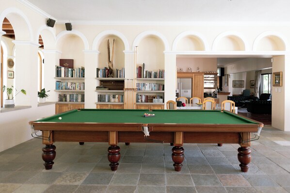 A pool table in a room with bookshelves, a fireplace, and a dining area.