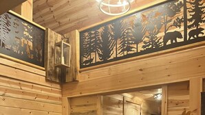 A wooden interior with a sofa, a door, and a wall with animal cutouts. - Luxury 3-bed hemlock log cabin Cave Run Lake area, with WiFi, gameroom, hot tub (West Liberty)