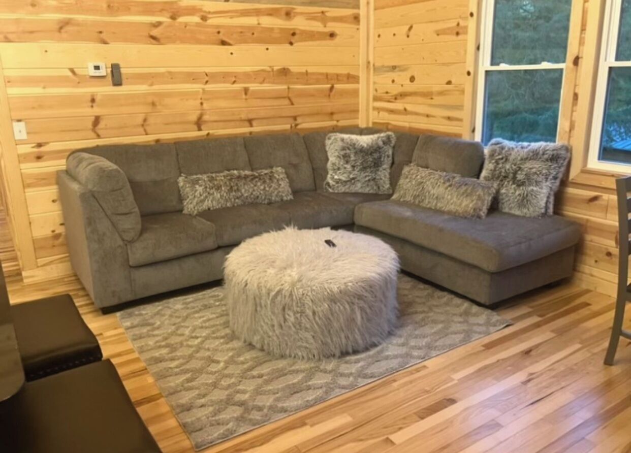 A cozy living room with a sectional sofa, fluffy ottoman, and a patterned rug.