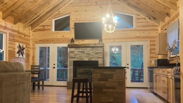 A spacious log cabin interior with a stone fireplace, wooden floors, and a large TV mounted on the wall. - Luxury 3-bed hemlock log cabin Cave Run Lake area, with WiFi, gameroom, hot tub (West Liberty)