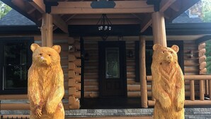 A wooden cabin with a porch featuring two bear sculptures. - Luxury 3-bed hemlock log cabin Cave Run Lake area, with WiFi, gameroom, hot tub (West Liberty)