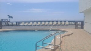 Una piscina amb una escala metàl·lica, un edifici blanc i una filera de gandules.