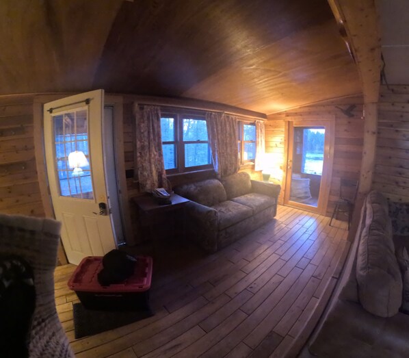 A cozy cabin interior with a wooden floor, a sofa, a door, and a window with curtains. - Moose Lake Hayward WI (Hayward)