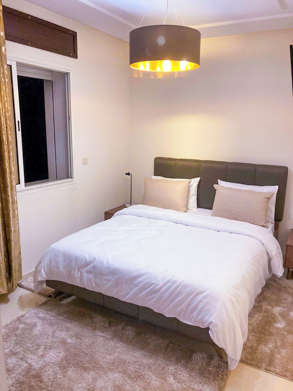 A bedroom with a bed, a nightstand, a lamp, and a window.