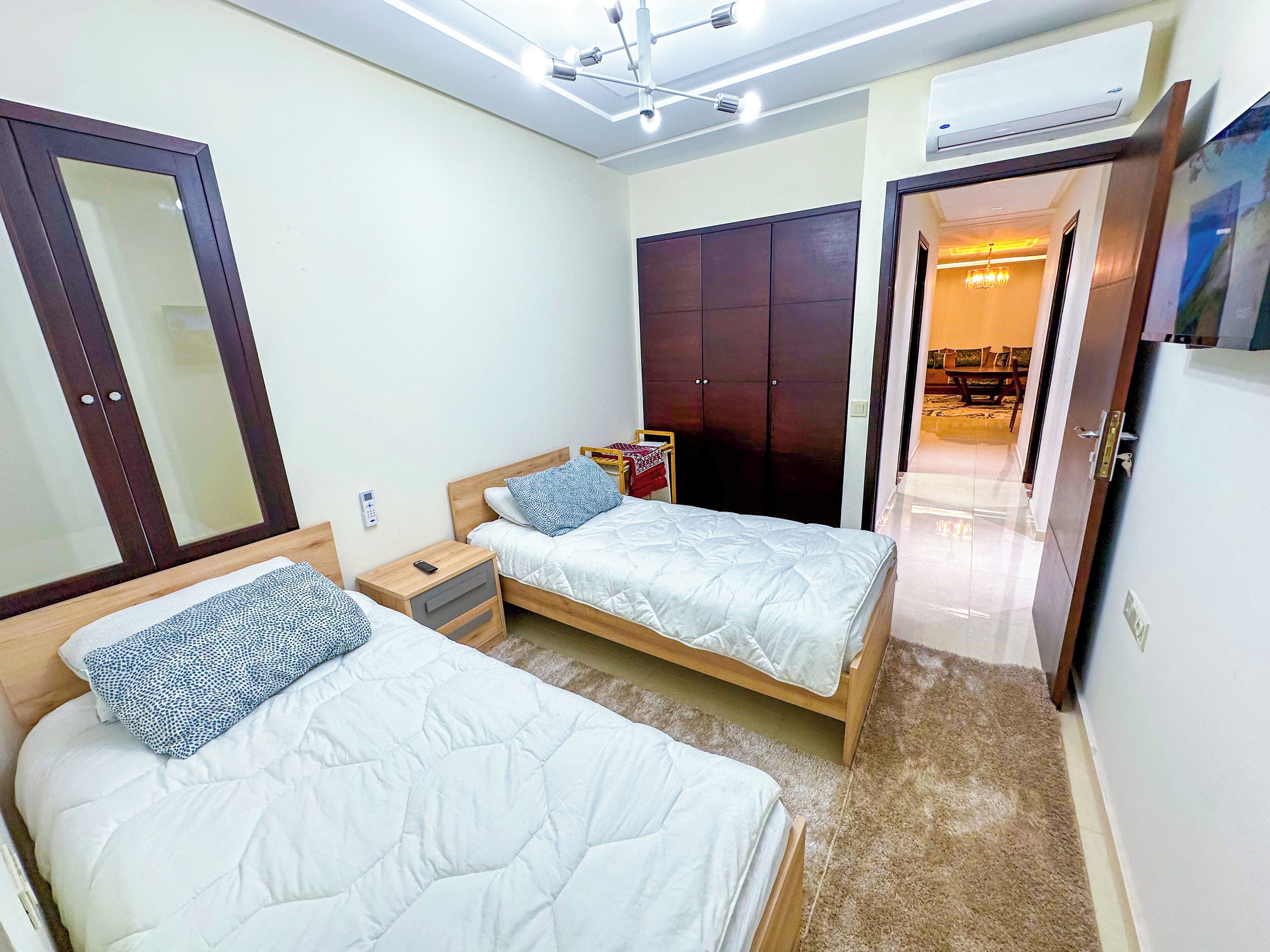 Een slaapkamer met twee bedden, een kledingkast, een spiegel, een nachtkastje met een telefoon en een airconditioning.