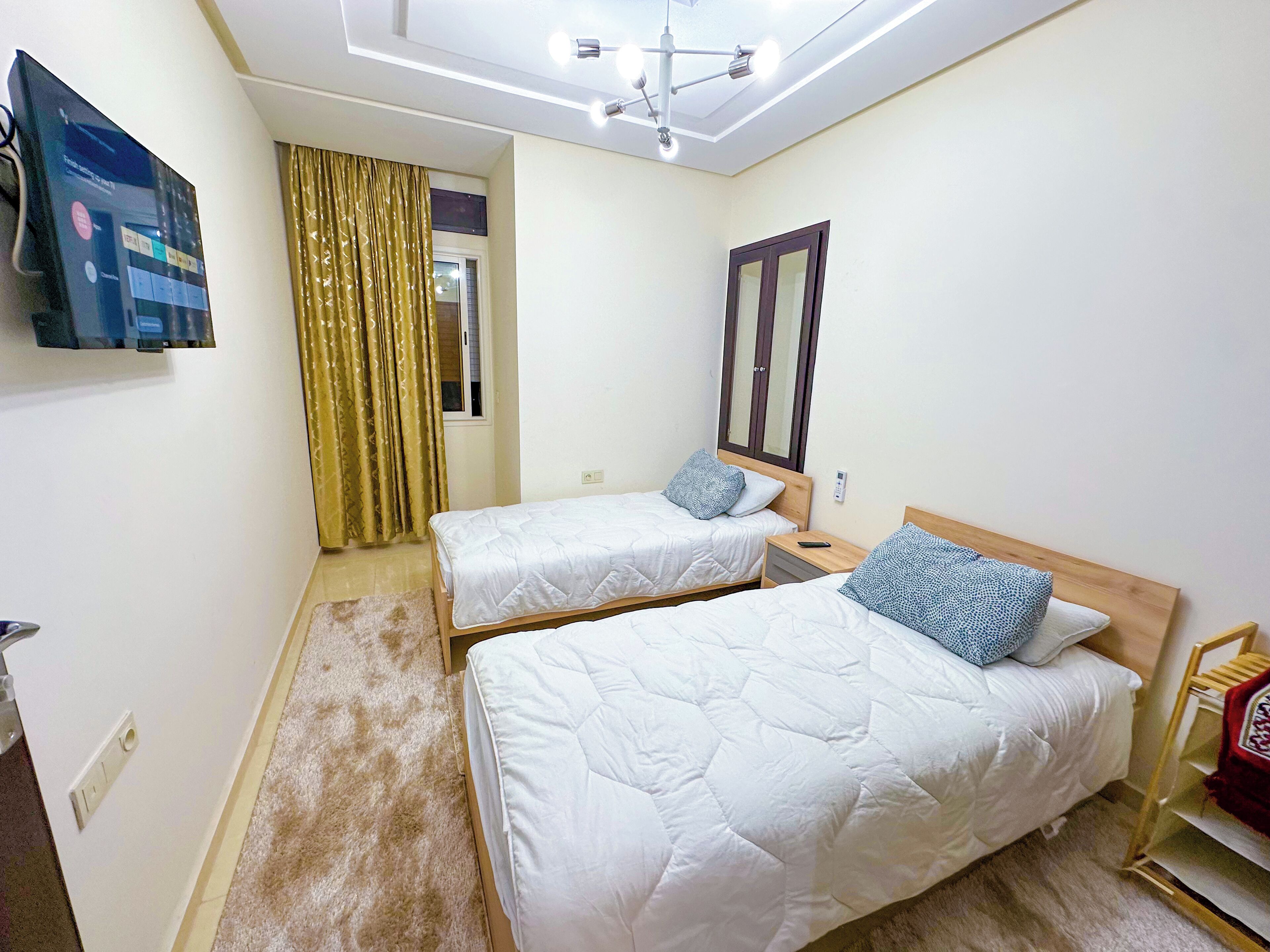 A hotel room with two beds, a TV, a mirror, and a ceiling light fixture.