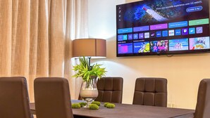 A hotel room with a flat-screen TV mounted on the wall displaying a streaming service interface. There is a dining table with four chairs and a potted plant on it. - Luxoria home - 2 min to corniche (Tangier)