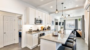 Una cocina moderna con armarios blancos, una isla central con taburetes de bar, microondas e iluminación colgante.