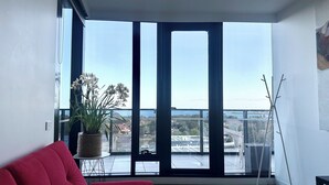 A modern living room with a red sofa, a potted plant, and a view of a cityscape through large windows. - luxury apartment with water views. Walking distance from beach (Port Melbourne)