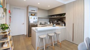 A modern kitchen with a central island, bar stools, and built-in appliances. - luxury apartment with water views. Walking distance from beach (Port Melbourne)