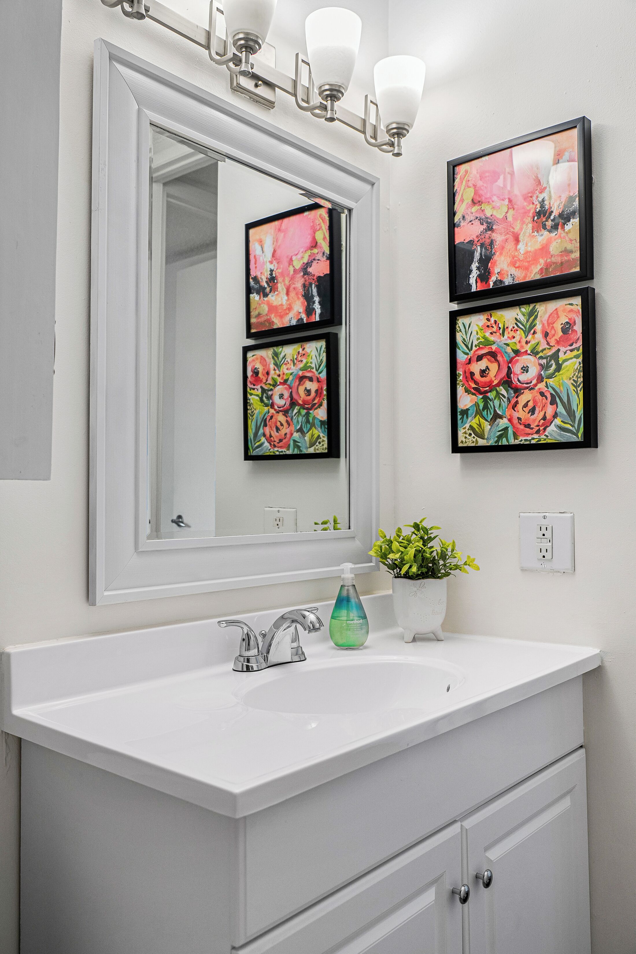 Une salle de bain avec un meuble-lavabo blanc, un grand miroir et deux tableaux floraux encadrés.