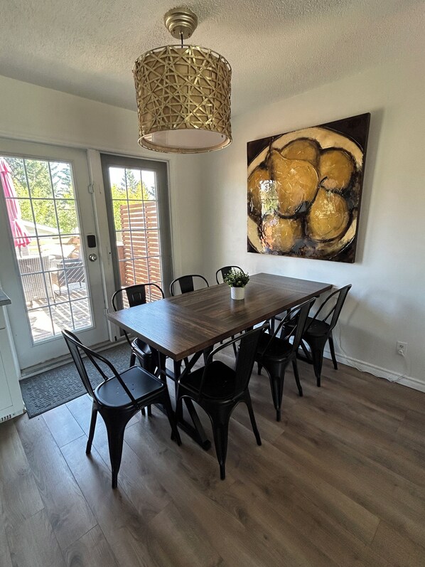 A dining area with a wooden table and chairs, a pendant light, and a large abstract painting on the wall. - Large Groups, Sleeps 16, AC, King Bed, Fire Pit, large patio. (Calgary)
