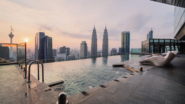 Ein Infinity-Pool auf dem Dach mit Blick auf eine Stadtlandschaft, darunter die Petronas Towers, sowie moderne Liegestühle.