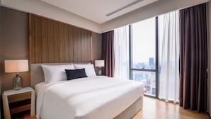 Ein Hotelzimmer mit einem großen Bett, zwei Nachttischen mit Lampen, Blick auf die Stadt durch große Fenster und einer Wandverkleidung aus Holz.