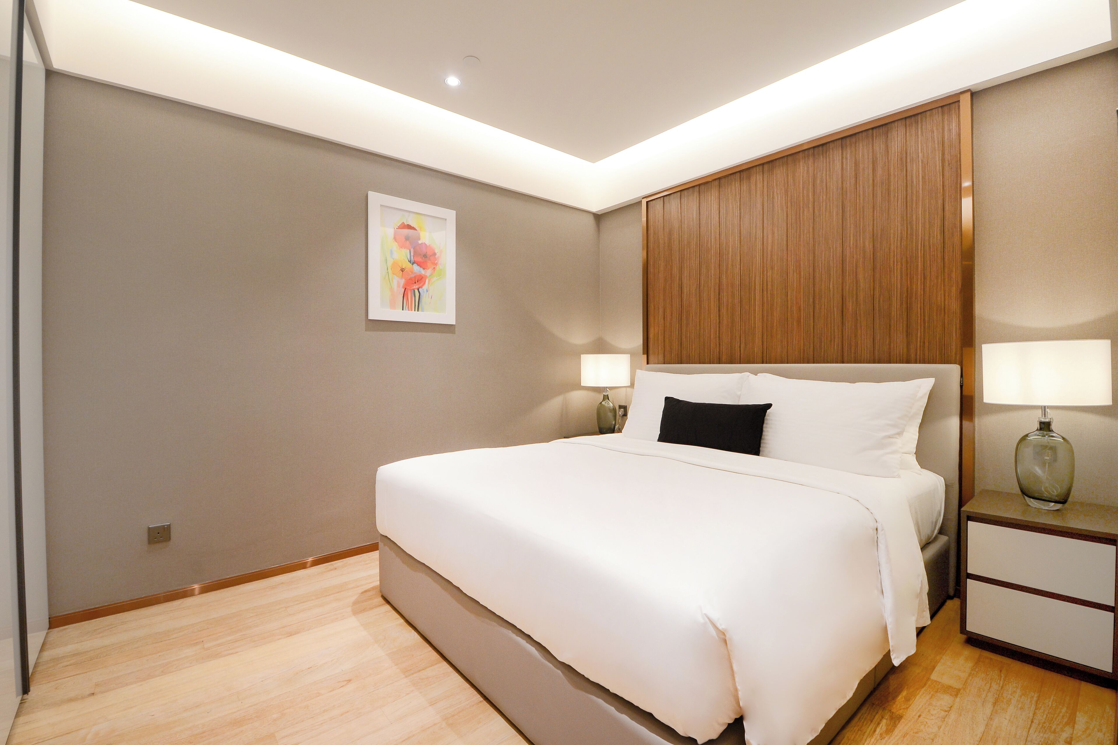 A modern hotel room with a large bed, two bedside lamps, a wooden headboard, and a single wall art piece.