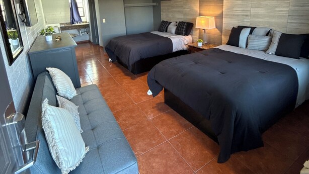 Quarto de hotel com duas camas, um sofá, uma pequena cozinha e um banheiro.