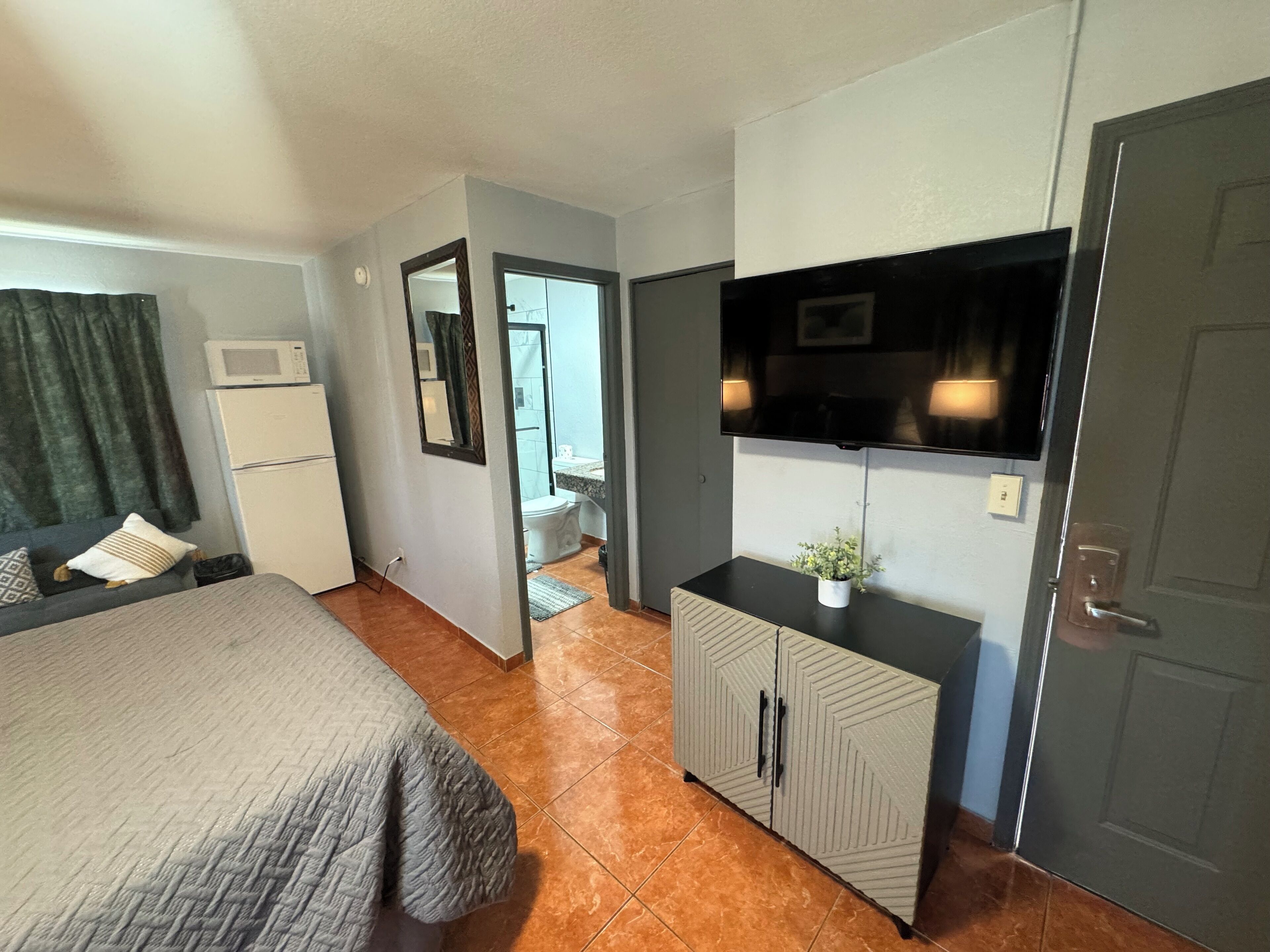 A hotel room with a bed, a TV mounted on the wall, a small cabinet, and a door leading to the bathroom.